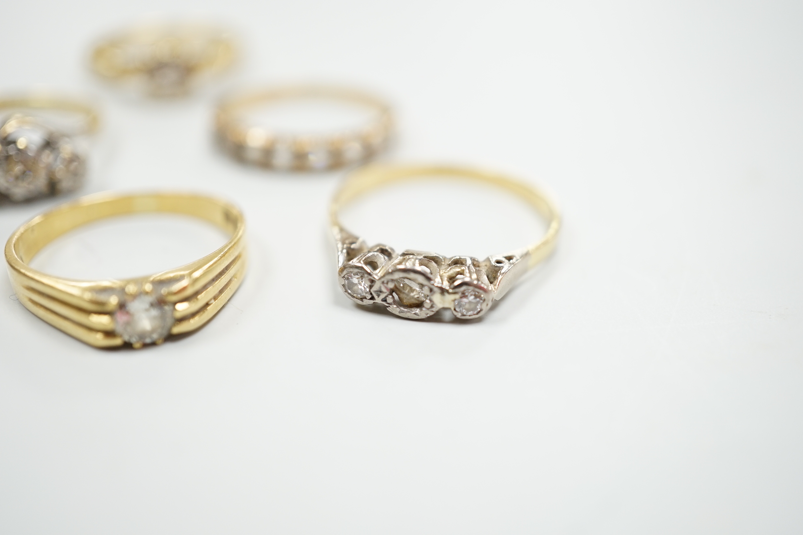 Six assorted gold dress rings, comprising an 18ct gold and platinum three stone ring, size O, an 18ct gold claw set solitaire diamond ring, size O, an 18ct gold illusion set solitaire diamond ring, size L, an 18ct gold t